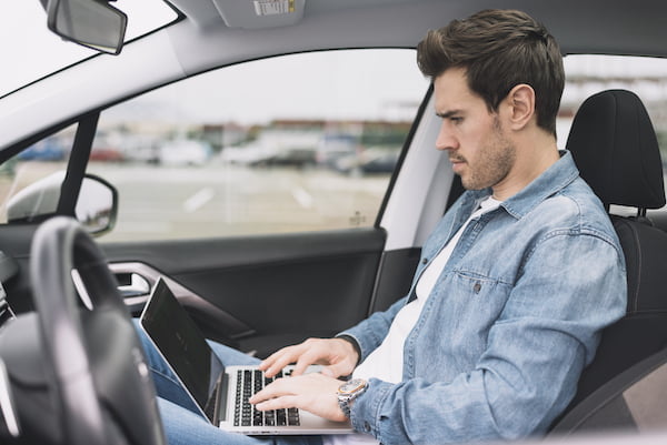 handsome young man sitting inside car using laptop